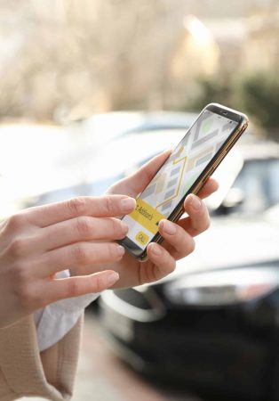 Woman ordering taxi with smartphone on city street, closeup